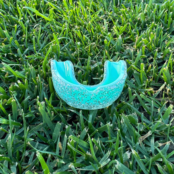 teal glitter mouthguard on grass
