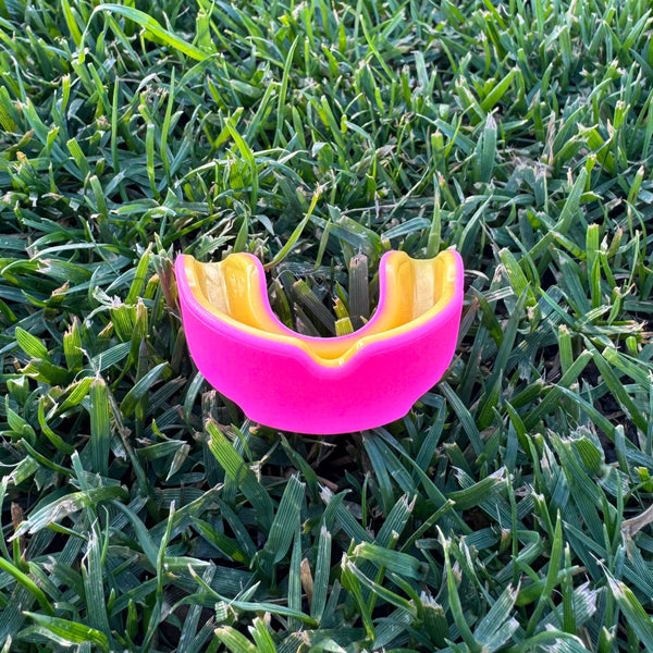 neon pink and orange mouthguard on grass